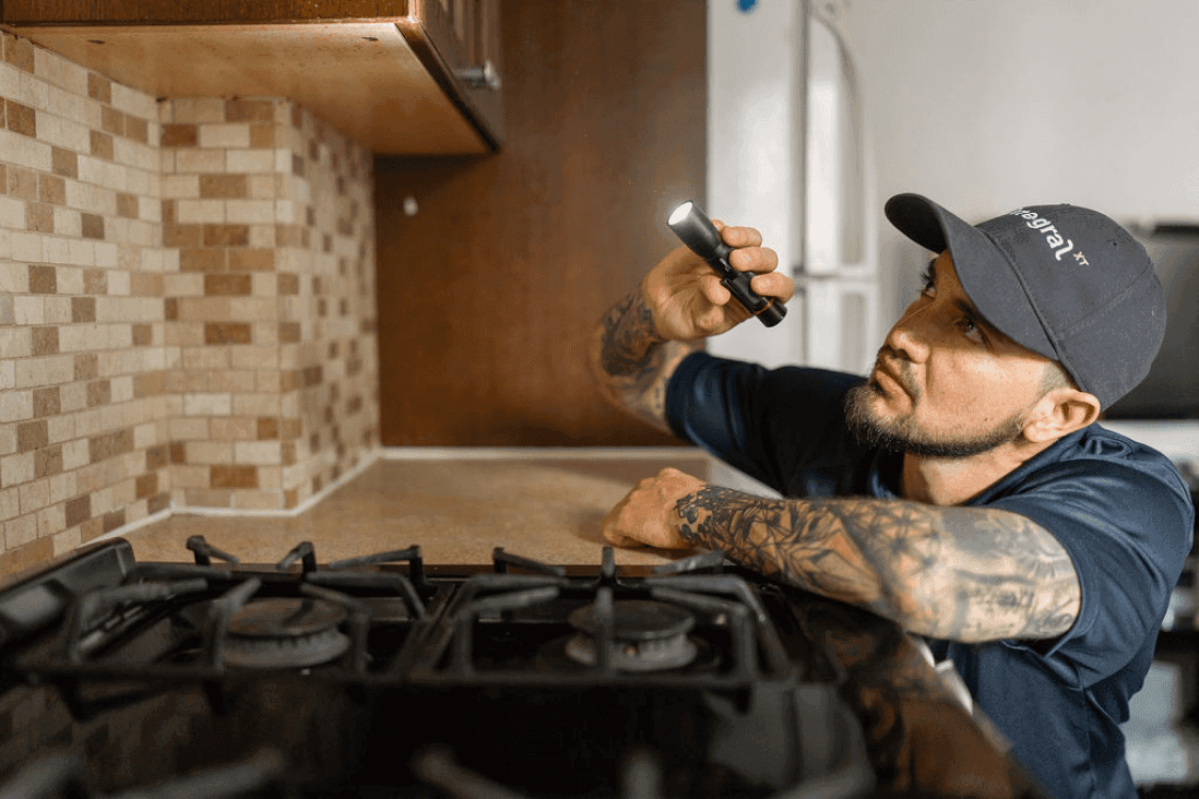 Exterminateur avec une lampe de poche entrain d'inspecter la cuisine d'un client